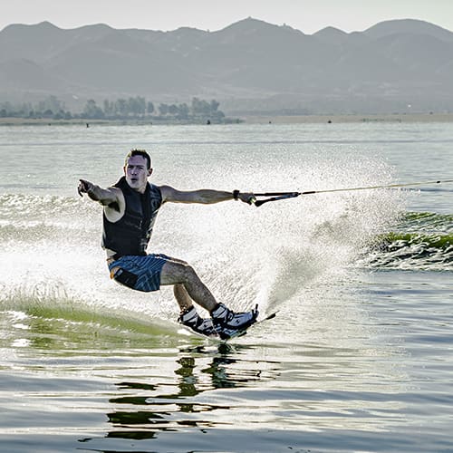A person is wakeboarding on a lake with mountains in the background.