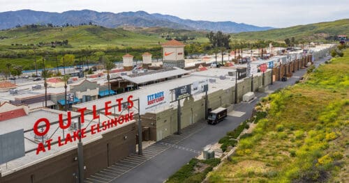 Aerial view of the Outlets at Lake Elsinore shopping center with various store signs and mountains in the background.