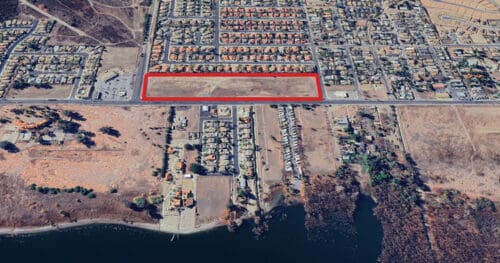 Aerial view of a residential neighborhood with a large rectangular empty lot outlined in red near a body of water.
