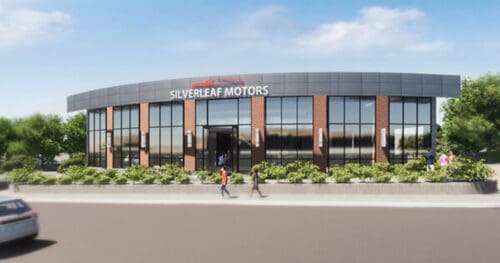 A modern car dealership building with large windows, labeled Silverleaf Motors, surrounded by greenery and people walking outside.