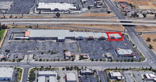 Aerial view of a shopping center with a large parking lot; one building near the upper right is outlined in red.