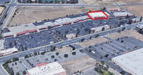 Aerial view of a shopping center with multiple parking lots and buildings; one building near the upper right is outlined in red.