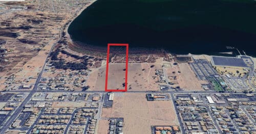 Aerial view of a coastal area with a rectangular section outlined in red, showing land near the water and surrounding buildings and infrastructure.